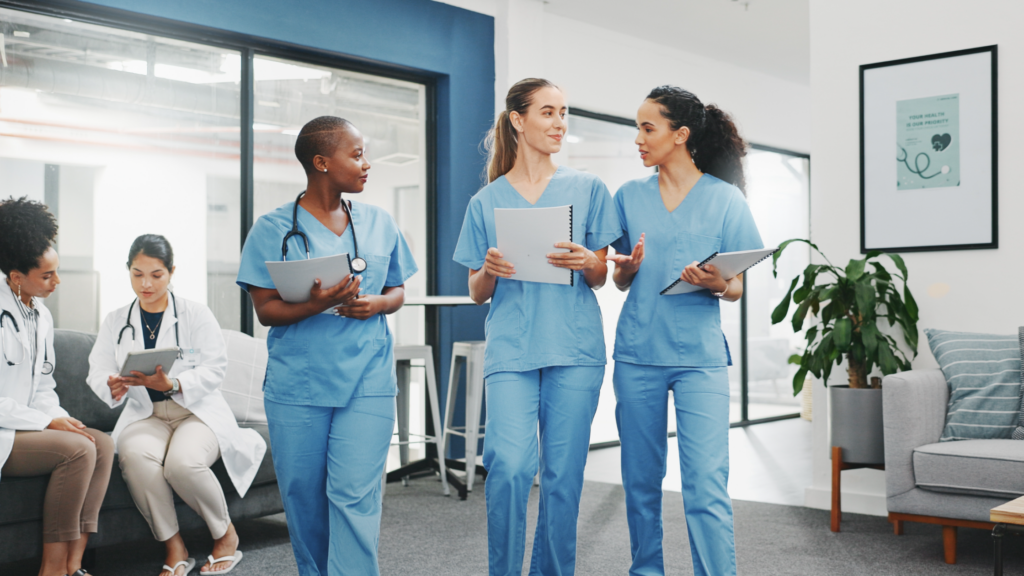 Three nurses in blue scrubs discussing patient care in modern medical clinic waiting room